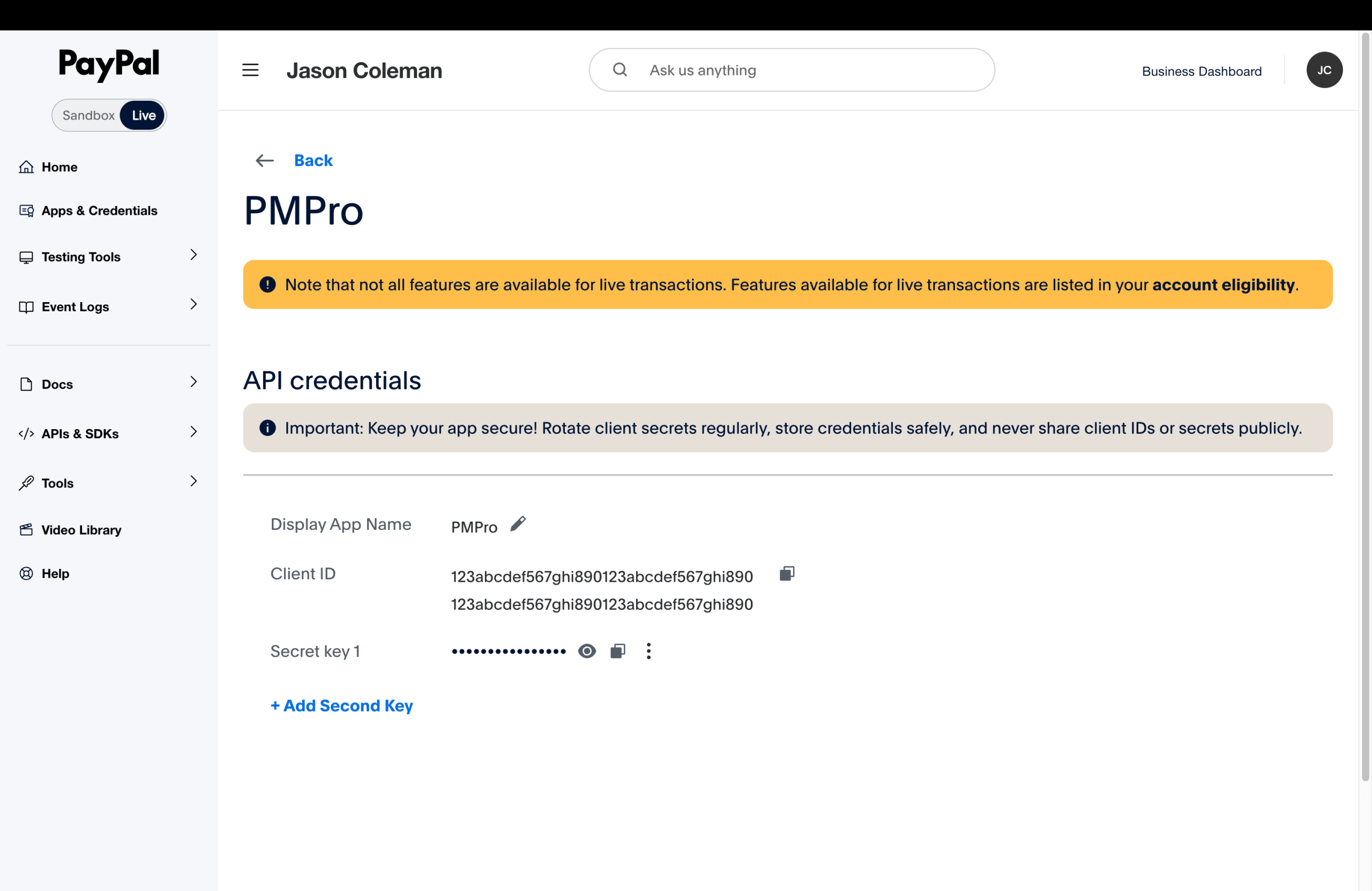 PayPal Developer Dashboard live app detail page for the PMPro app, showing the API credentials section with a masked Client ID and masked Secret key. A notice reminds users that not all features are available until account eligibility is confirmed.