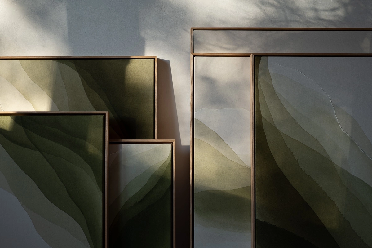 Four of Christina Hohenwarter's framed paintings leaning against a wall in layered greens and earth tones, with sunlight and tree shadows falling across them.